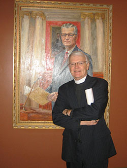 The Rev. Dennis Johnson '60, serving as Chaplain of the Minnesota House, stands in front of the gubernatorial portrait of Harold LeVander '32. (Photo by Erin Wilken '02)